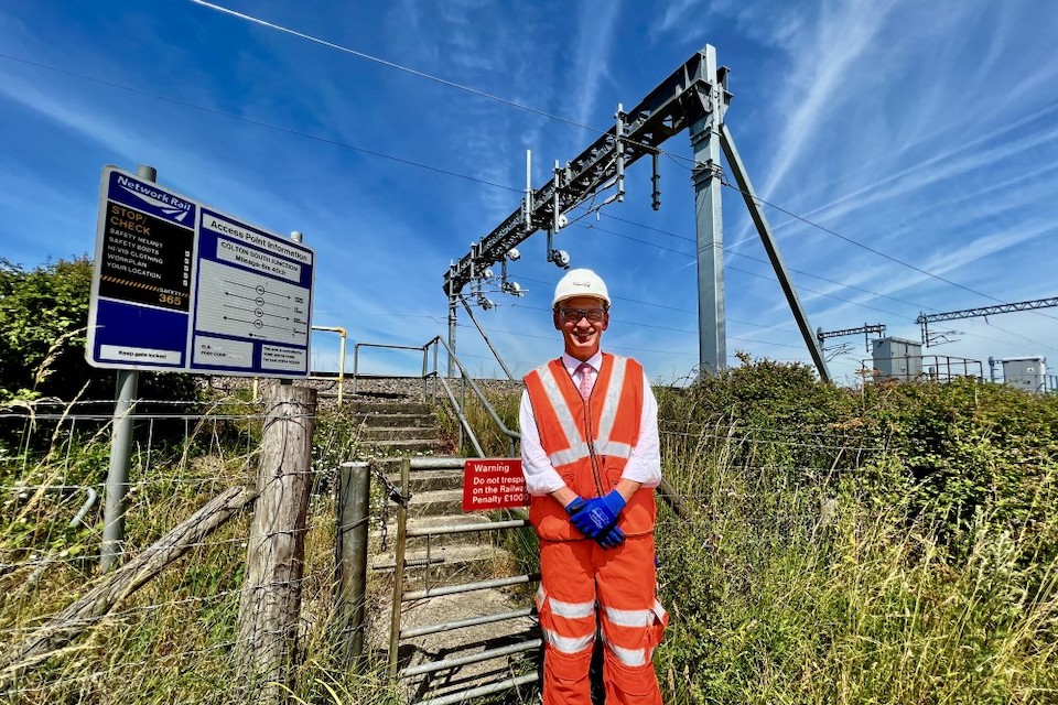 Proud engineer in orange safety suit standing in front of catinery wires